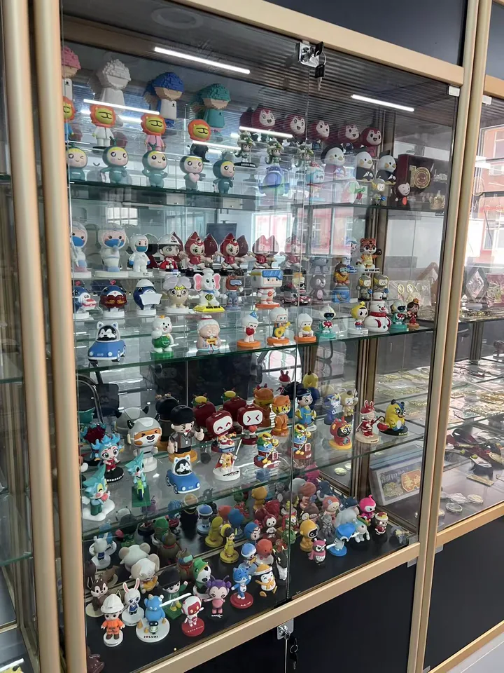 A studio display cabinet filled with custom PVC figures, mascots, pendants, and cultural products